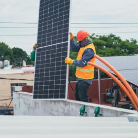A technician in safety gear installs a solar panel on a rooftop, promoting renewable energy.